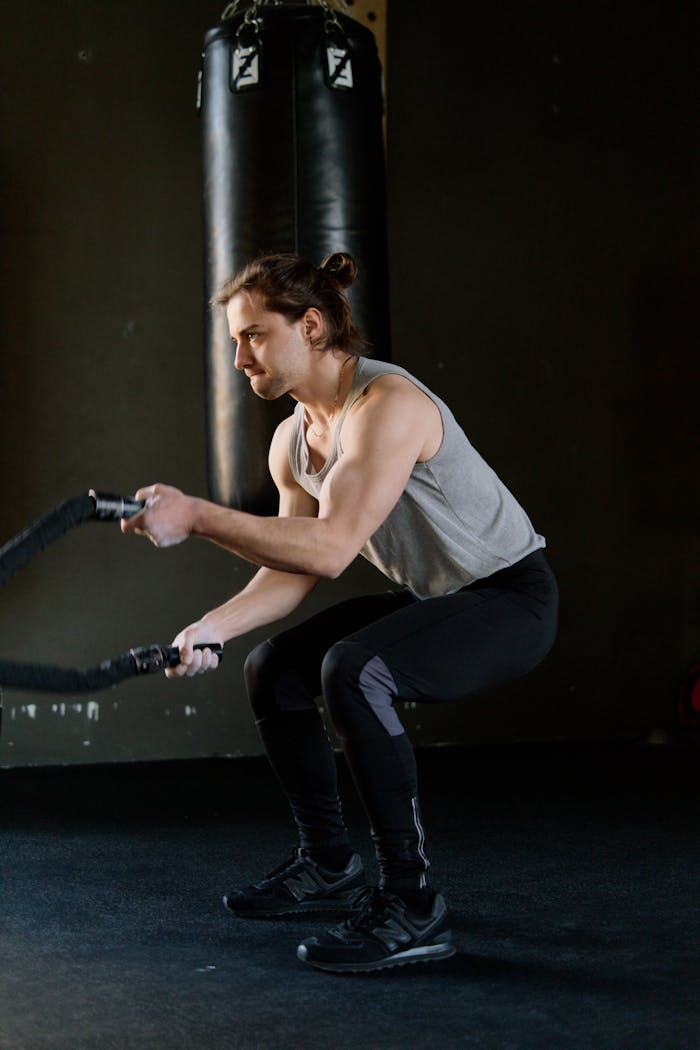 Athletic man doing intense battle rope workout inside a gym to build muscle and stamina.